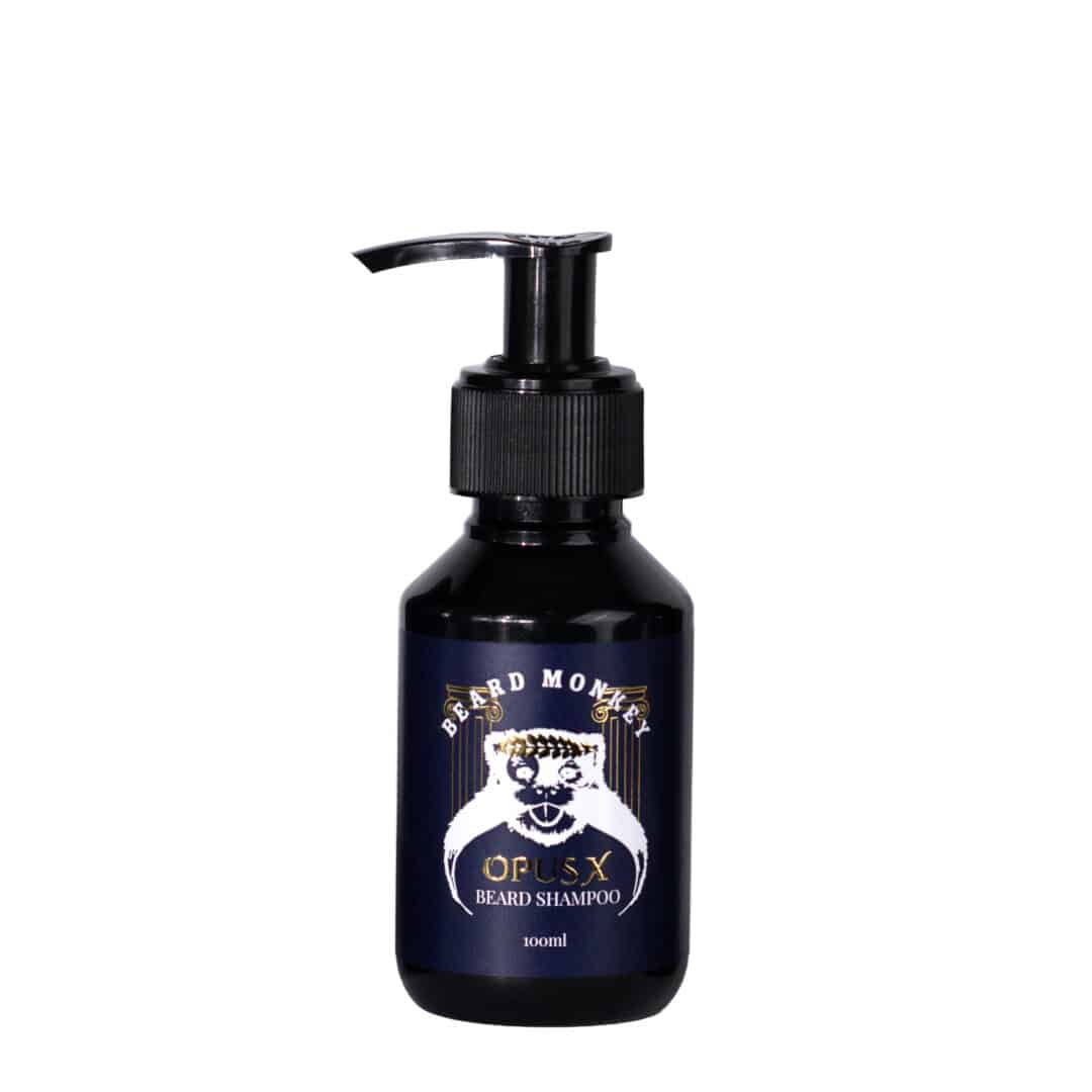 Beard Monkeys skäggschampo I doften OPUS X. En svart pumpflaska om 100ml med mörkblå etikett och vit text. Etiketten är dekorerad med Beard Monkey apan som bär en lövkrona av guld och har två pelare med antik design i guld bakom sig.